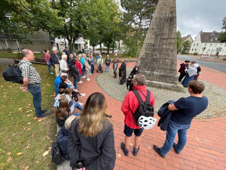 Eine Personengruppe bei einer Führung vor einem Denkmal